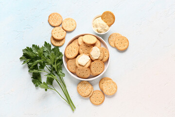 Tasty crackers with bowl of sauce and parsley on light blue background