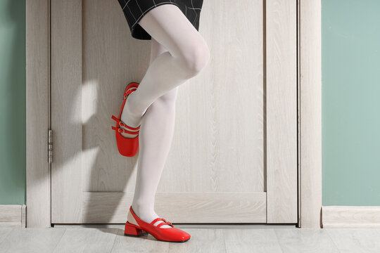 Female legs in stylish red shoes near wooden door