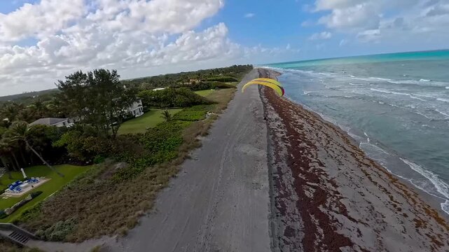 Aerial view of the turquoise ocean meeting the sandy beach, a paraglider soaring above the coast, Jupiter Island, Florida, United States.