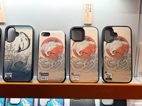 Smartphone cases featuring Japanese ukiyo-e style artwork of cranes and koi fish on display at a retail store for iPhone 16 and SE models - Tokyo, Japan, October 15, 2024