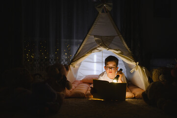 Obraz premium Boy reading book inside teepee tent at night