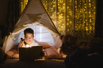 Obraz premium Boy reading story with flashlight in teepee at night