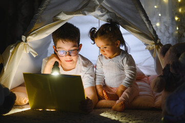 Obraz premium Children reading bedtime story using flashlight in tent