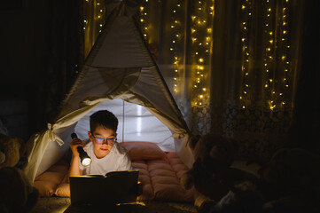 Obraz premium Boy reading storybook in teepee with flashlight