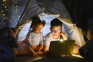 Obraz premium Children reading book with flashlight in cozy tent