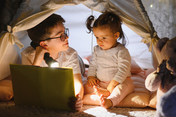 Obraz premium Children reading story book with flashlight in tent