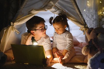 Obraz premium Children reading book with flashlight inside blanket fort