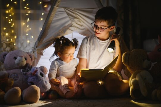 Older brother reading bedtime story to younger sister inside tent