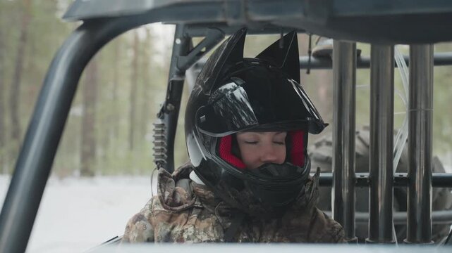 Atv rider snowy forest helmet closeup, driver scans trail from utv cabin, glossy black helmet with red liner, breath fog in cold air, camouflage jacket, steel rollcage frame, focused eyes, prestart