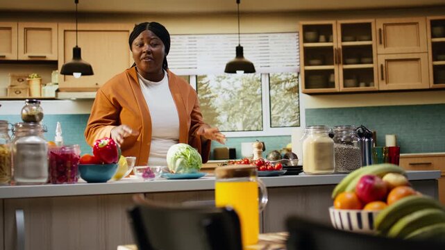 Black woman chef recording a cooking tutorial video at the kitchen counter under natural light. Food influencer shows meal prep and salad preparation steps for her vlog channel.