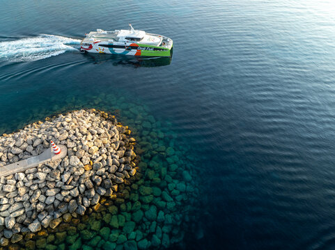 Mgarr Harbor, Malta - 08 June 2025: Aerial view of a vibrant ferry cutting through the deep blue sea, leaving a frothy white wake near the rocky pier.