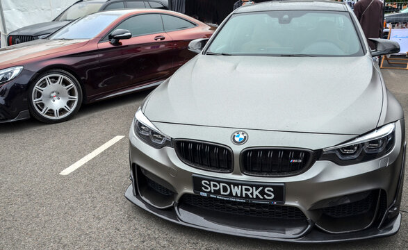 Matte silver BMW M3 (F80) with aggressive carbon fiber aero components is parked at an outdoor event. A high-performance German sedan with a sharp, modern aesthetic