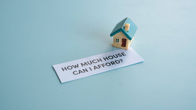 Miniature house and a slip of paper with text asking how much house can I afford regarding real estate financing.