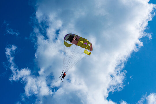 Cox's Bazar, Bangladesh - 18 August 2023: Aerial view of a vibrant parasailor suspended against a backdrop of fluffy white clouds and a deep blue sky.