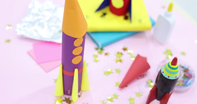 Toy and handmade rockets on light pink background, closeup