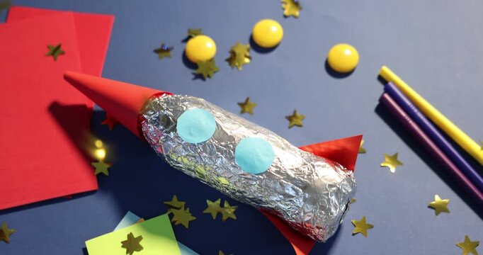 Star shaped confetti falling over handmade rocket on blue background, closeup