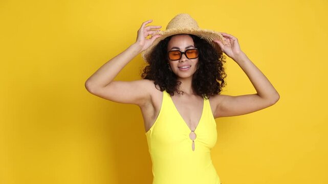 Woman wearing swimsuit, hat and sunglasses on yellow background