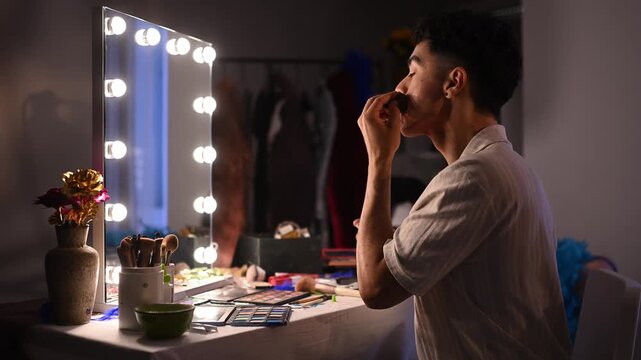 Drag queen applying foundation and contouring in front of a brightly lit vanity mirror before a show performance