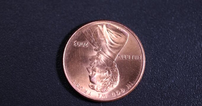 one American cent on a black plastic surface while rotating around its axis, an old worn American coin one cent, close up