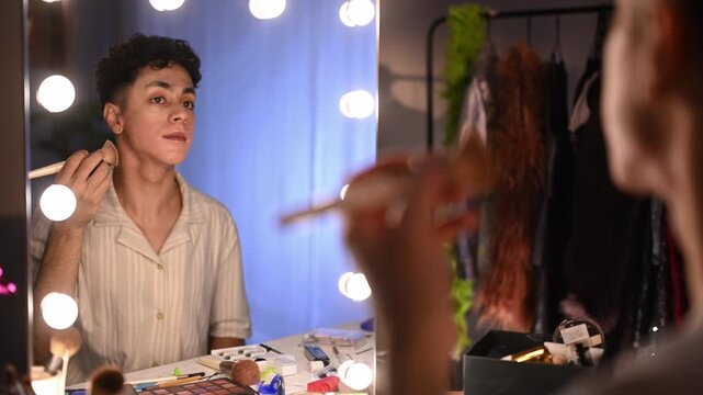 Young drag queen applying makeup and foundation while preparing for a show in a dressing room backstage