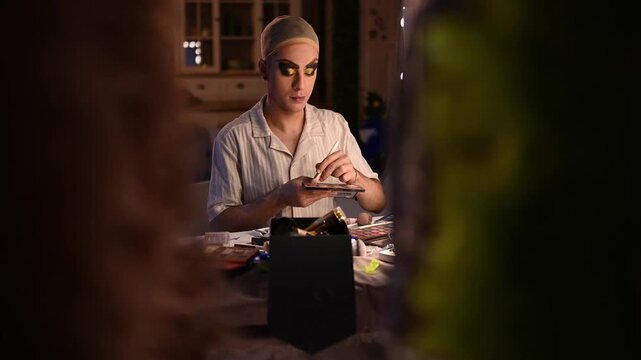 Professional drag queen applying theatrical eyeshadow makeup in front of a mirror backstage before a performance