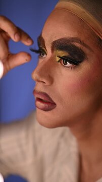 Close up of a drag queen carefully applying long, false eyelashes, perfecting an elaborate and colorful stage makeup look before a show