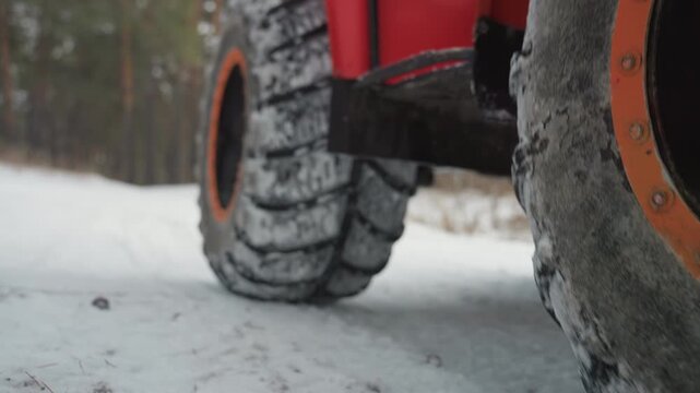 Red atv tires on icy road, lowangle closeup showing heavy tread packed with snow, orange rim and rugged suspension, pine forest backdrop, cold gritty atmosphere conveying extreme offroad grip