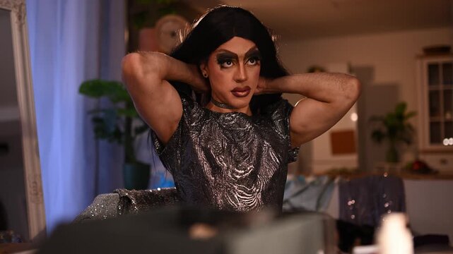 Confident drag queen with dramatic makeup and a shiny outfit dancing and posing in a dressing room before a show