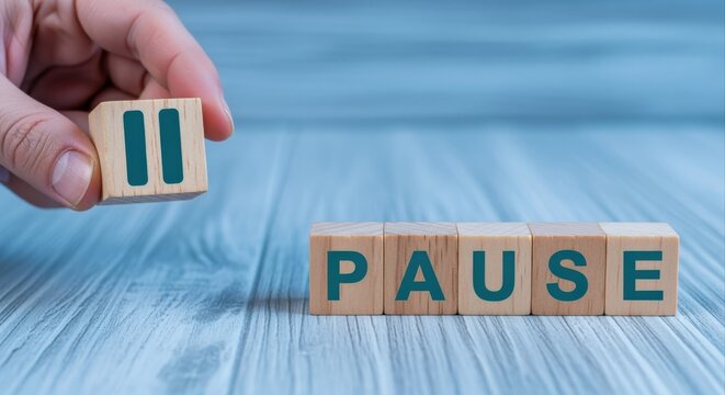 Hand placing wooden block with pause symbol next to word PAUSE on striped surface