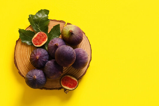 Wooden board with fresh ripe figs on yellow background