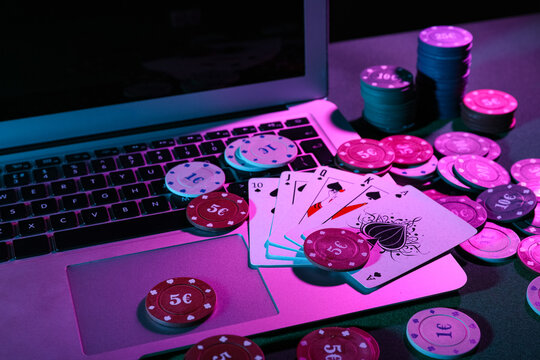 Laptop with playing cards and poker chips on green table, closeup