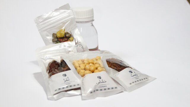 Hajj and Umrah souvenirs including dates, nuts, raisins, almonds, Zamzam water and prayer beads coming out of a paper gift bag, isolated on white background