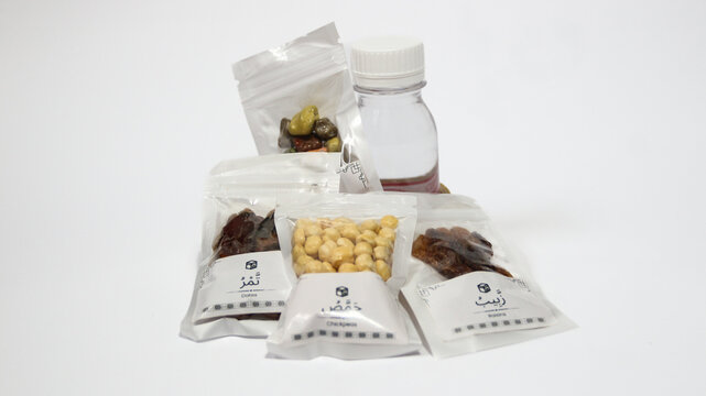 Hajj and Umrah souvenirs including dates, nuts, raisins, almonds, Zamzam water and prayer beads coming out of a paper gift bag, isolated on white background