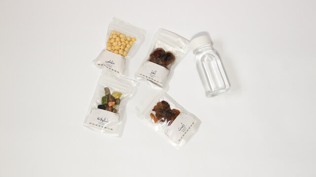 Hajj and Umrah souvenirs including dates, nuts, raisins, almonds, Zamzam water and prayer beads coming out of a paper gift bag, isolated on white background