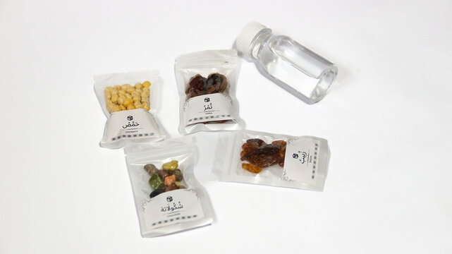 Hajj and Umrah souvenirs including dates, nuts, raisins, almonds, Zamzam water and prayer beads coming out of a paper gift bag, isolated on white background