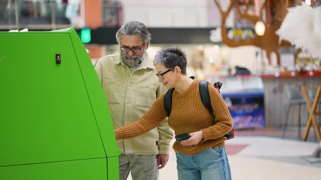 Mature couple withdrawing cash money from an atm machine in a shopping mall
