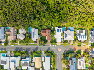 Aerial view of a modern residential neighborhood with many homes featuring solar panels and pools, bordering a lush green forest on the Sunshine Coast, Queensland. © Mujie