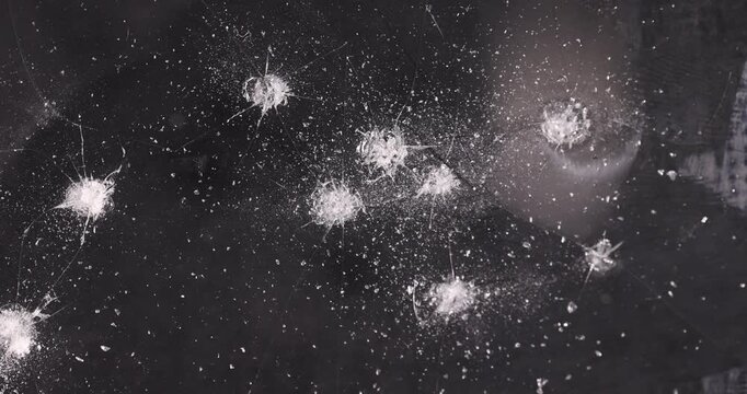 thin broken glass on black paper, dents on the glass where it broke, white cracks and completely broken places on the glass on a black uneven background
