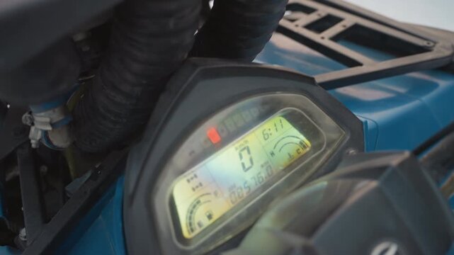 Atv dashboard closeup showing digital display, gloved hand adjusts controls during preride inspection on blue quad, speedometer reads zero, illuminated indicators and odometer visible, plastic