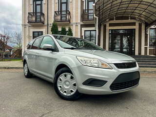 Naklejka premium Silver compact car parked in front of a large building on a cloudy day in the city
