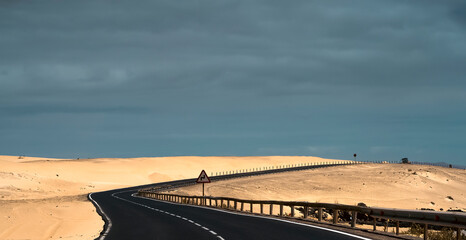 Naklejka premium An asphalt road among desert with sandy dunes.
