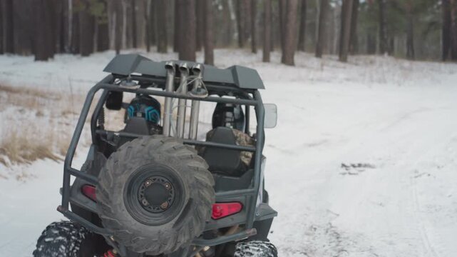 Guide inspecting map for winter ATV trip. Driver with helmet prepares UTV for snowy forest journey. Spare tire and map checked before starting peaceful winter ATV excursion in snow