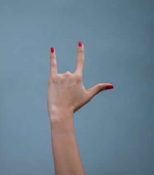Mano femenina con u&ntilde;as rojas haciendo gesto de amor y lenguaje de se&ntilde;as sobre fondo neutro minimalista