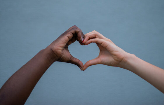 Manos de diferentes tonos de piel formando un coraz&oacute;n sobre fondo neutro, s&iacute;mbolo de amor, diversidad e inclusi&oacute;n