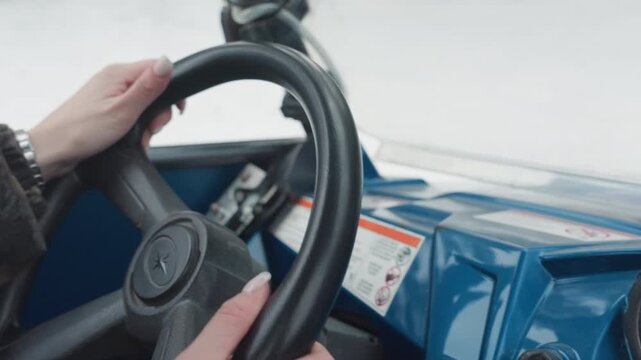 Hands on atv steering wheel guiding trail turns, camouflage jacket and gloves grip textured rim, blue console and dashboard visible, precise throttle and brake adjustments for extreme offroad
