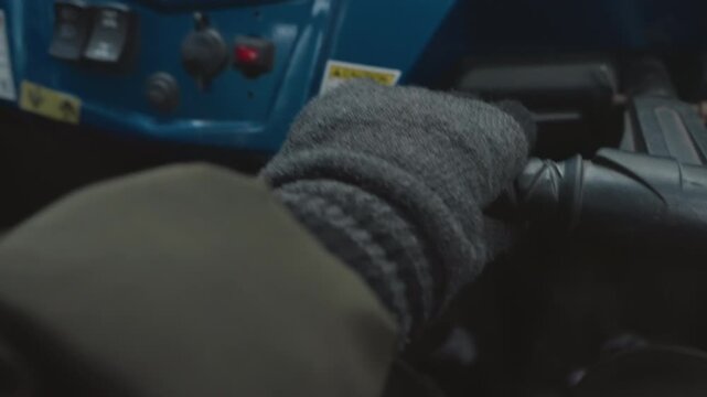 Gloved hand on atv throttle closeup blue dashboard knit glove textured grip on handlebar low light precise throttle input cold trail navigation cabin perspective showing cautious offroad handling