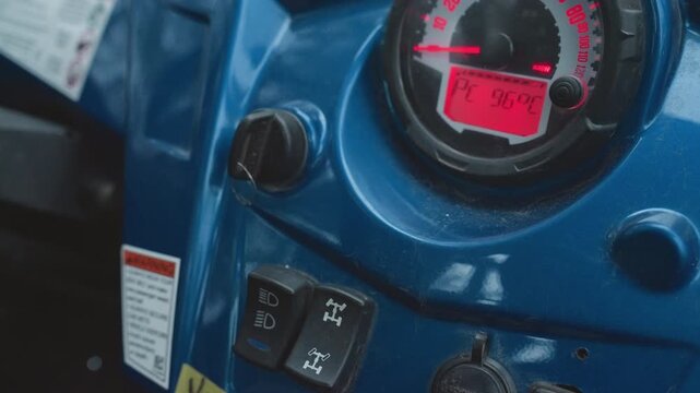 Closeup atv dash ignition hand turning key, blue console and digital gauge lighting, switches and knob in focus, rider preparing vehicle, preride inspection vibe with mechanical tension and outdoor