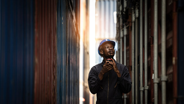 Worker inspecting container cargo at shipping port, African American male in logistics, transportation and export industry