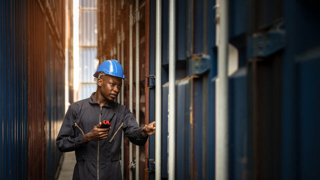 Worker inspecting container cargo at shipping port, African American male in logistics, transportation and export industry