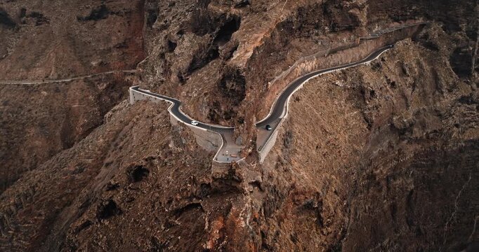 Winding mountain road viewpoint in the Masca region, Tenerife. Dramatic volcanic landscape, cars navigating the sharp turns of the challenging route in huge rocks. Aerial perspective, drone flight